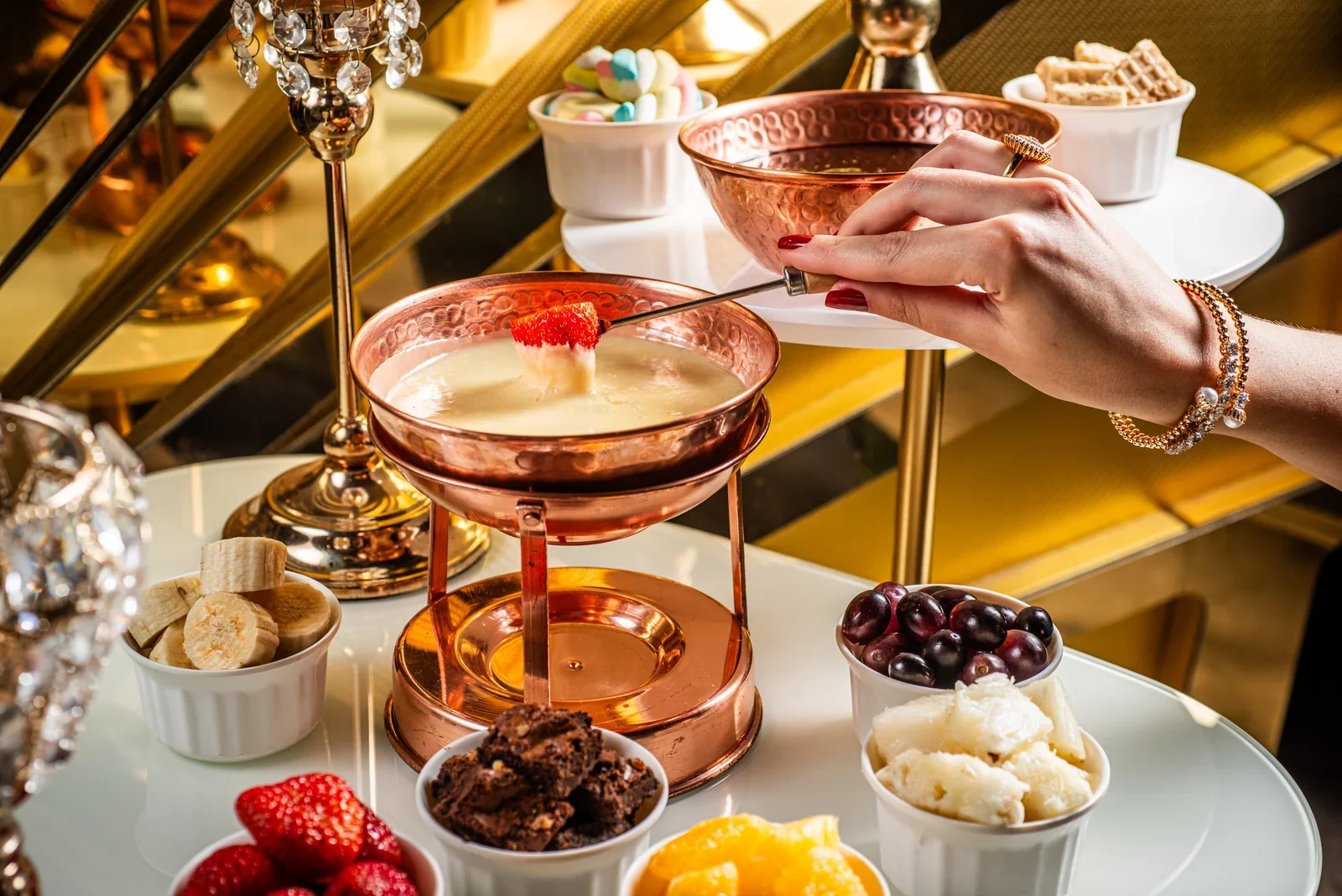 Morango mergulhado no fondue doce, com frutas e acompanhamentos